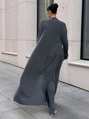 Person wearing a long dark gray dress walking on a sidewalk.