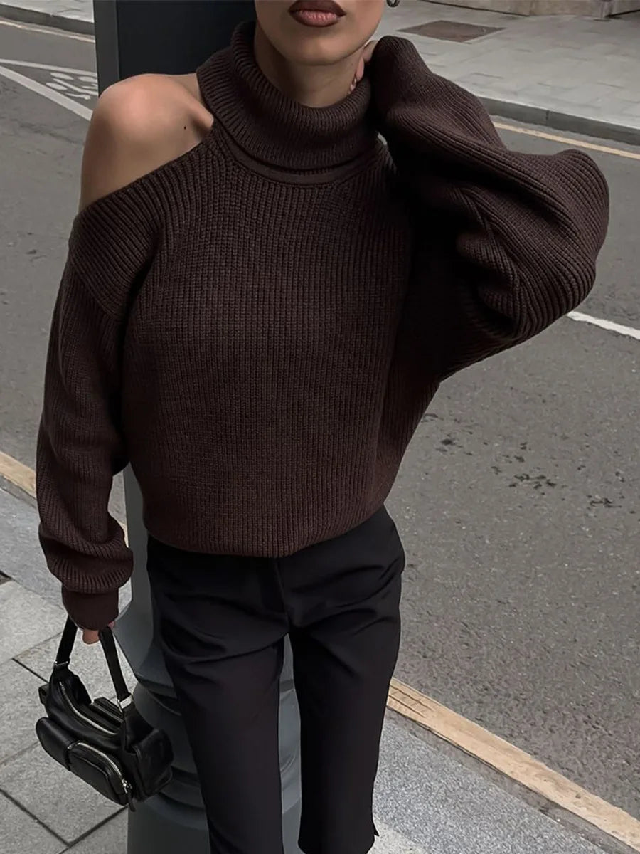 Person wearing a brown off-shoulder sweater and black pants on a street.