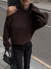 Person wearing a brown off-shoulder sweater and black pants on a street.
