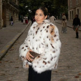 Woman wearing a white fur coat with black and brown spots on a city street.