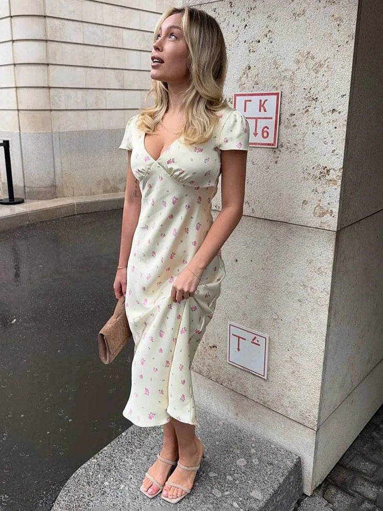Woman in a white floral dress standing against a wall with a sign.