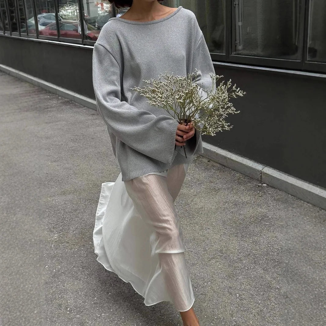 Person wearing a gray sweater and white pants holding flowers on a street.
