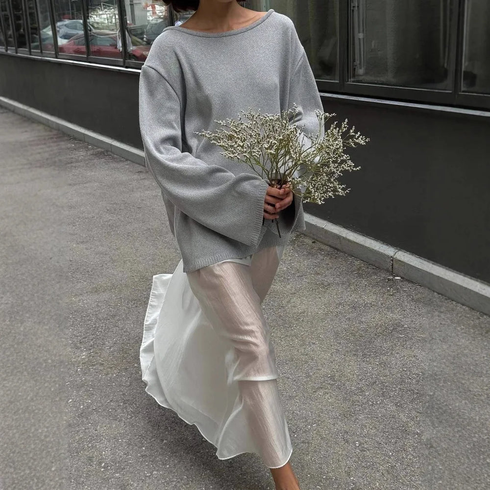 Person wearing a gray sweater and white pants holding flowers on a street.