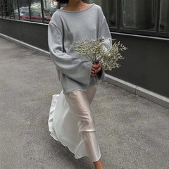 Person wearing a gray sweater and white pants holding flowers on a street.
