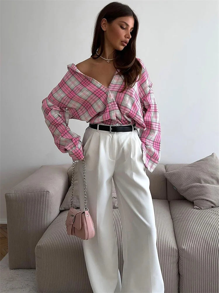 Woman wearing a pink plaid shirt and white pants in a living room setting.
