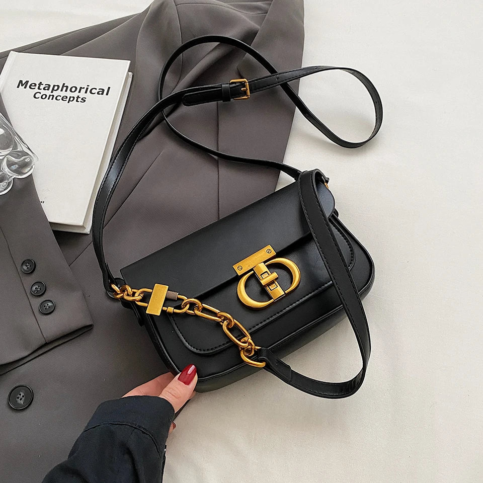 Black handbag with gold chain and clasp on a gray coat with a book underneath