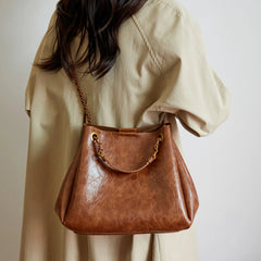 Brown leather handbag held by a person wearing a beige shirt against a plain background