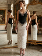 Back view of a woman in a black beaded V-neck sleeveless top with lace-up closure and a white ruched floor-length skirt.