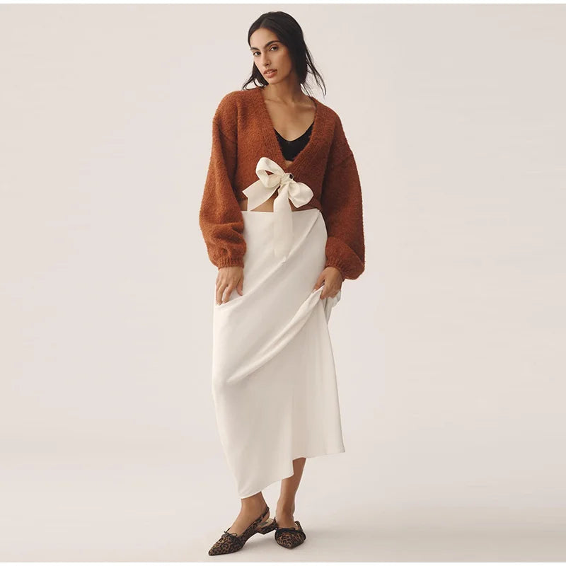 Woman wearing a brown sweater and white skirt with a bow on a plain background