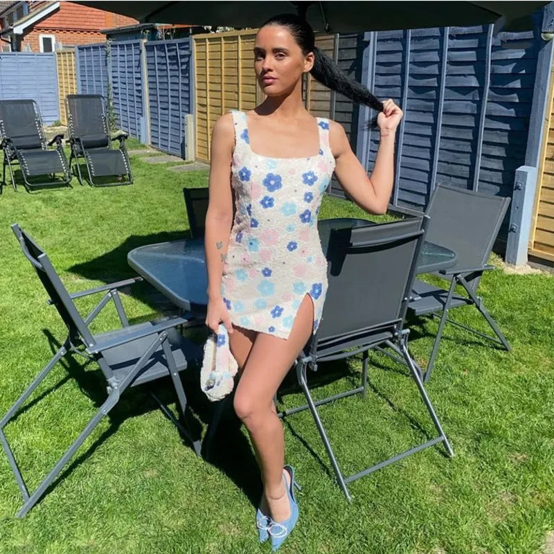 Woman in a floral dress standing outdoors on a grassy area with chairs and tables.