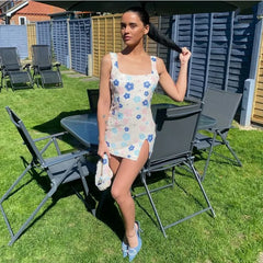 Woman in a floral dress standing outdoors on a grassy area with chairs and tables.