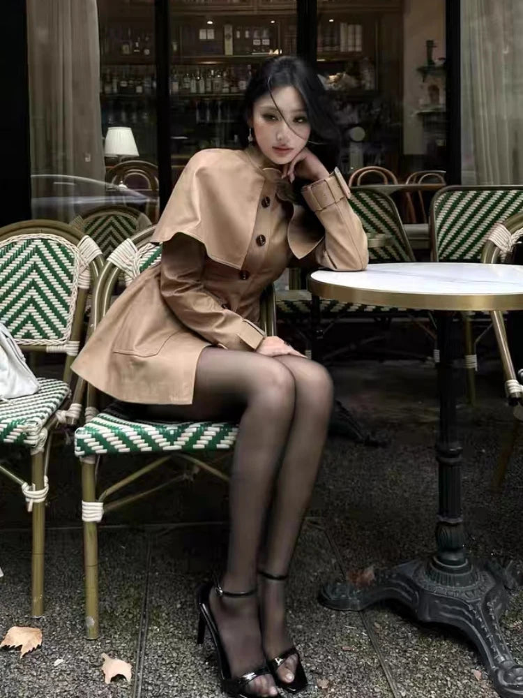 Woman in a beige coat sitting at an outdoor cafe table.