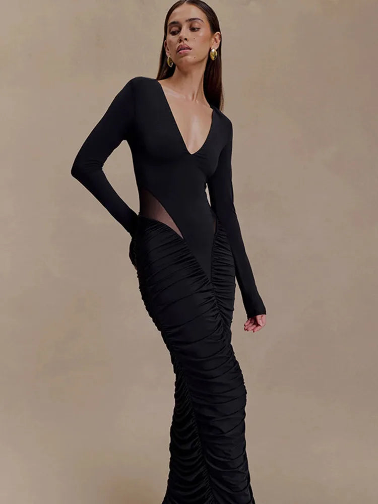 Woman wearing a black dress with a deep neckline and ruched details on a beige background