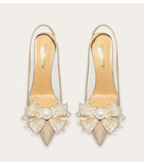 Pair of high-heeled shoes with decorative bows and pearls on a light background