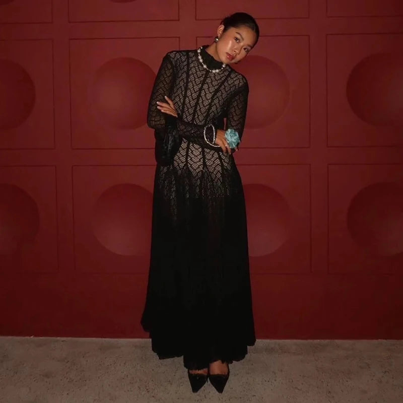 Woman in a black lace dress standing against a red wall.