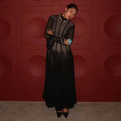 Woman in a black lace dress standing against a red wall.