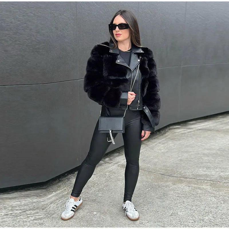 Woman wearing a black fur jacket, black leggings, and white sneakers against a gray wall.