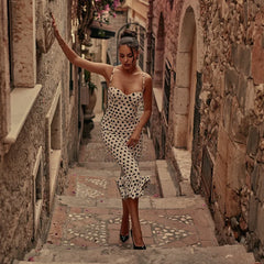 Woman in a polka dot dress walking down a narrow stone alleyway.