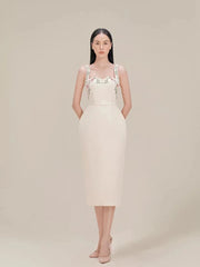 Woman wearing a white dress with floral straps against a beige background