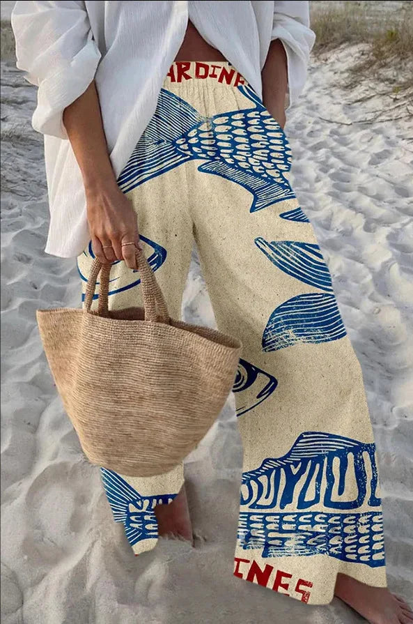 Person wearing blue and white patterned pants with a woven bag on a sandy background