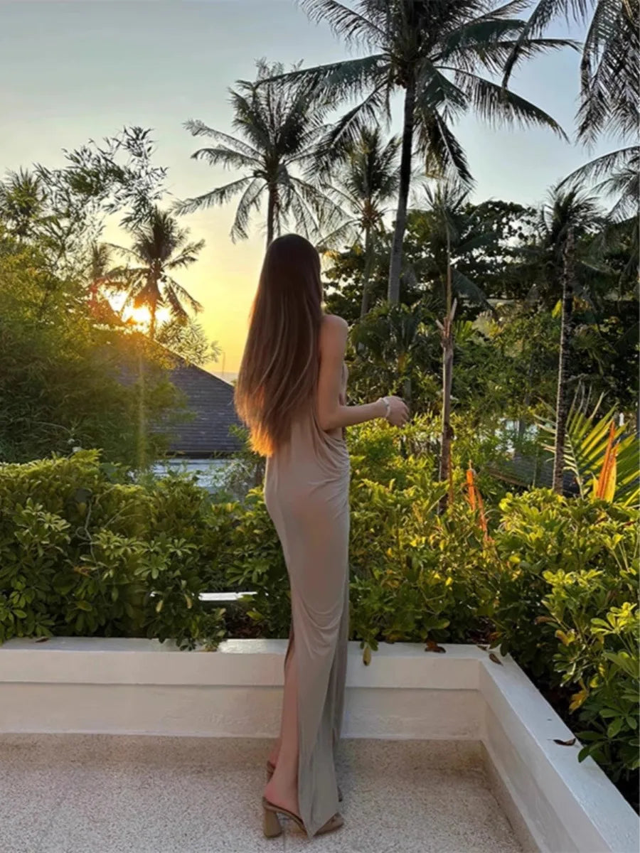 Woman in a long dress standing on a balcony with palm trees and sunset in the background