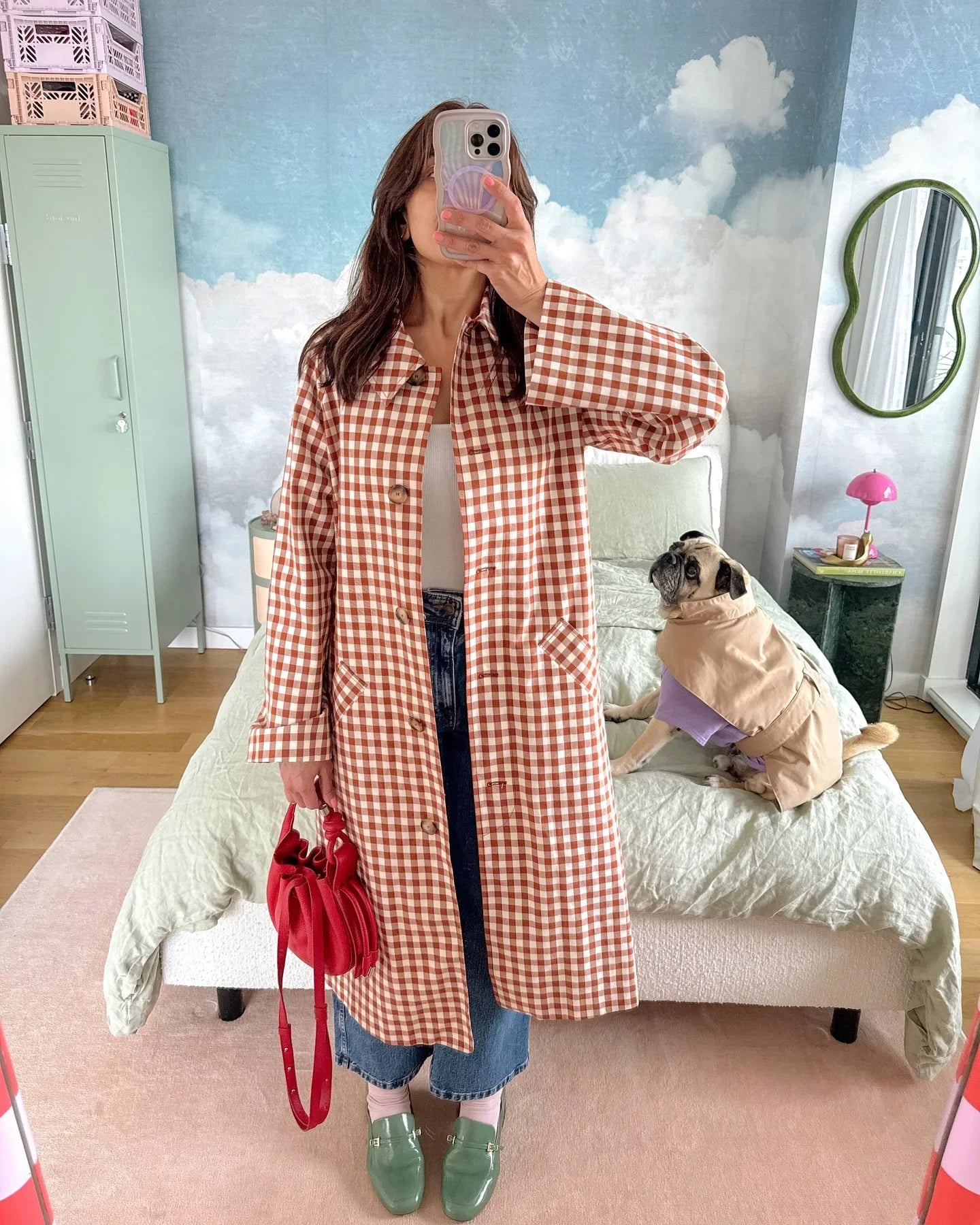 Person wearing a red and white checkered coat in a room with a dog on a bed.