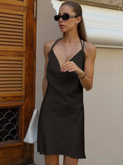 Woman wearing a black slip dress and sunglasses against a neutral wall.