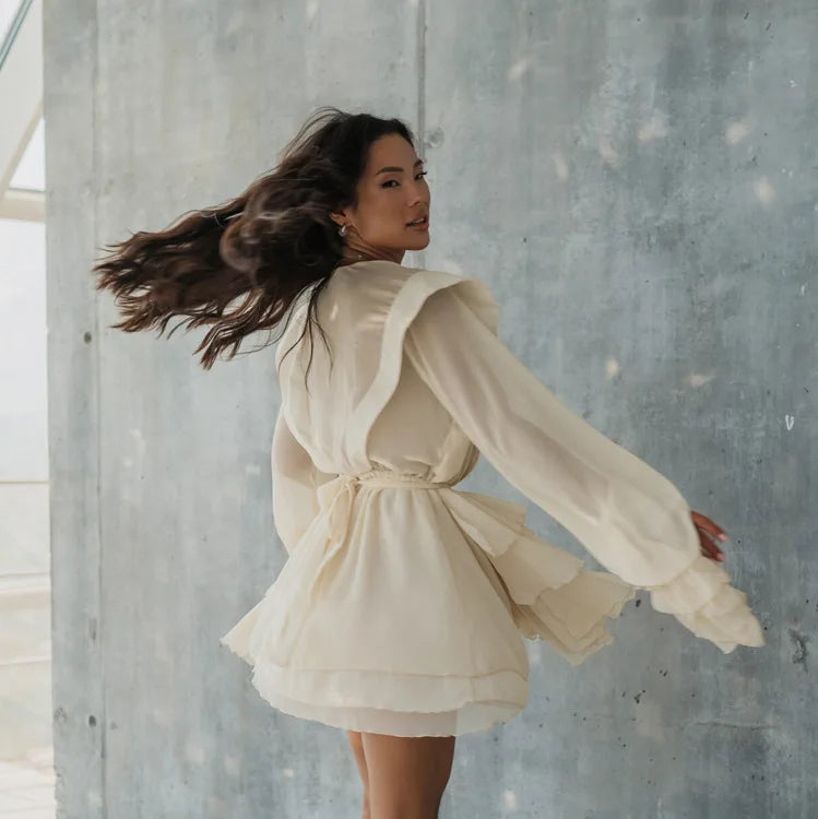 Woman in a beige dress standing against a concrete wall.