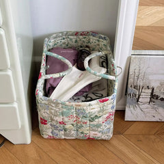 Floral-patterned laundry basket with clothes on a wooden floor next to a radiator.