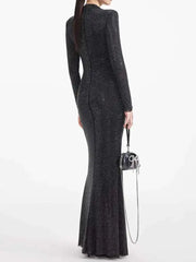 Woman wearing a long black dress holding a matching handbag on a white background