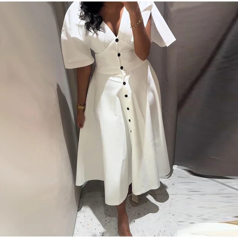 White dress with black buttons worn by a person against a neutral background