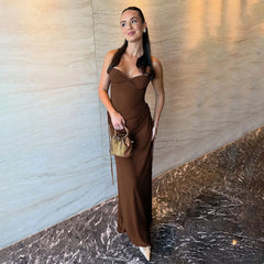 Woman in a brown dress holding a gold handbag against a marble wall.