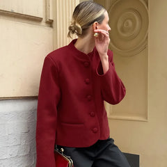 Woman in a red jacket sitting against a beige wall.