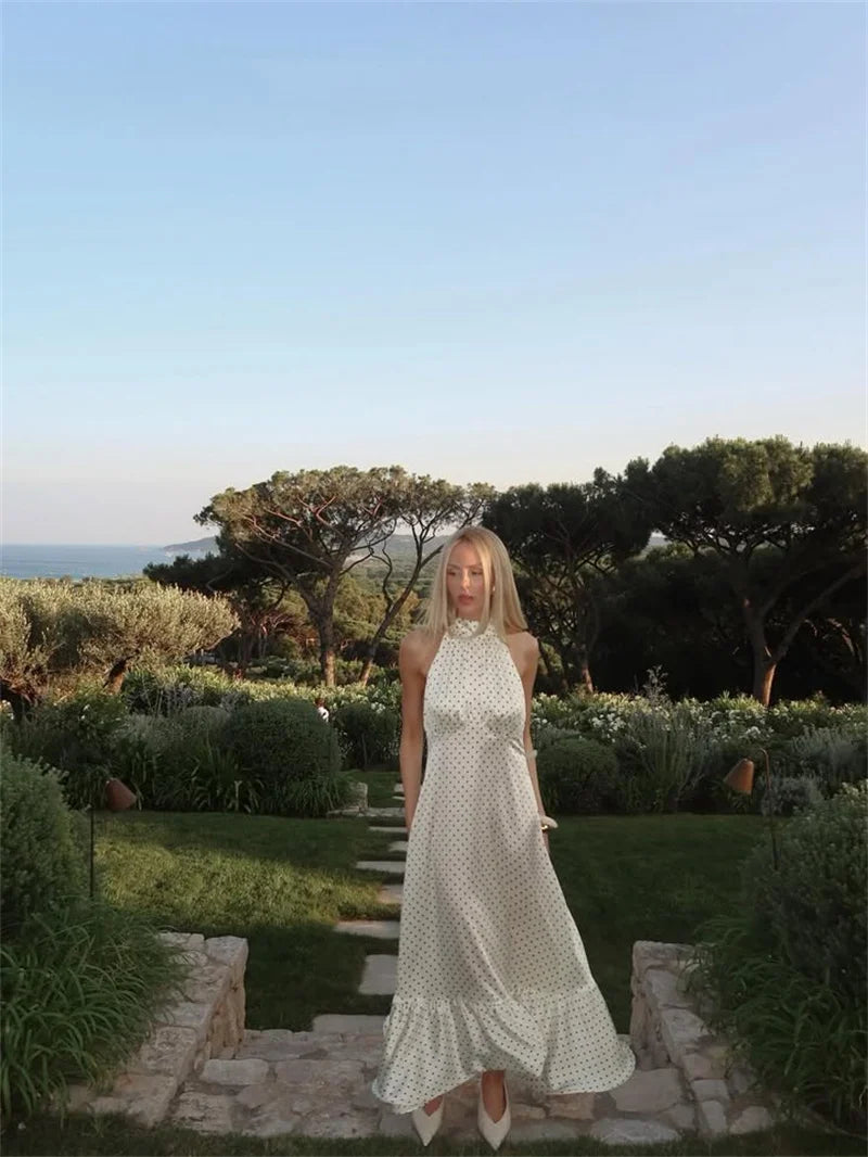 Woman in a white dress standing on a garden path with trees and sky in the background