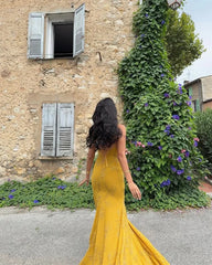 Woman in a yellow dress standing in front of a stone building with greenery.