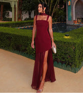 Woman in a burgundy dress standing outdoors with greenery and a pool in the background