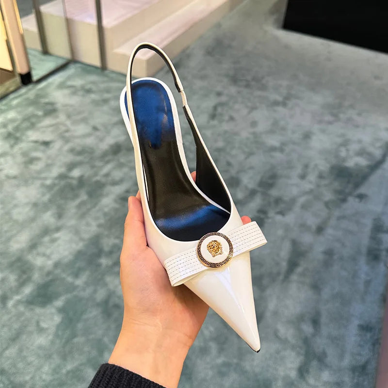 White pointed toe slingback heels with a bow detail and gold metal accent held in hand