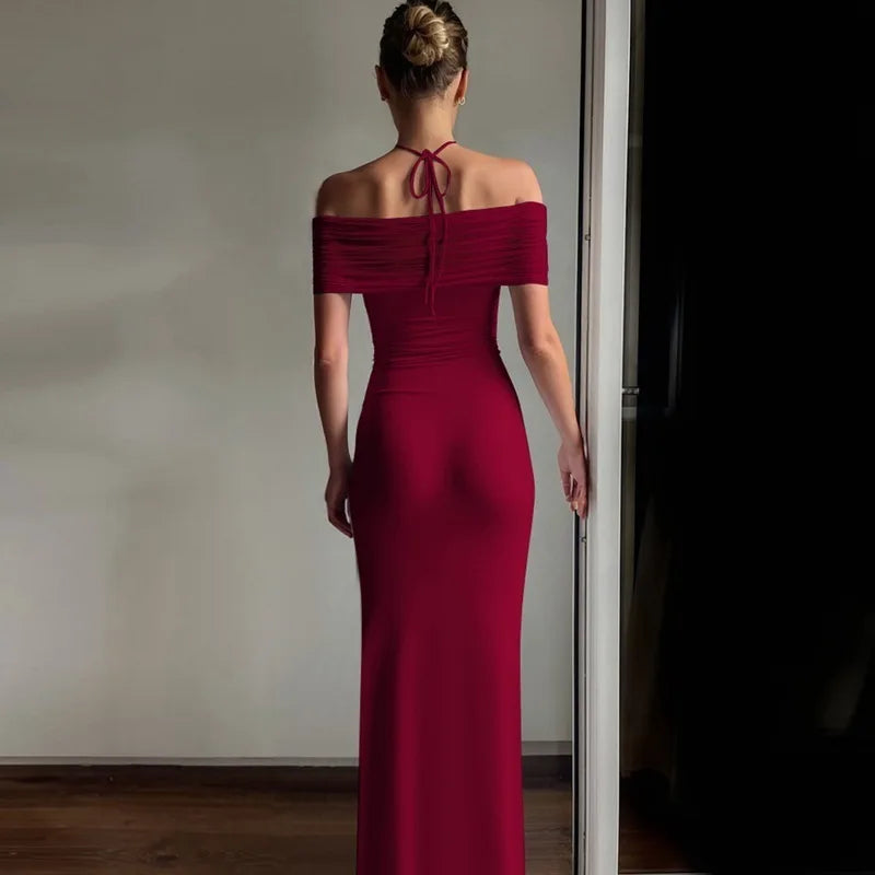 Woman in a red off-shoulder gown standing in a room with a neutral wall.