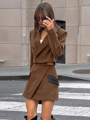 Woman taking a selfie wearing a brown coat and skirt set on a city street.