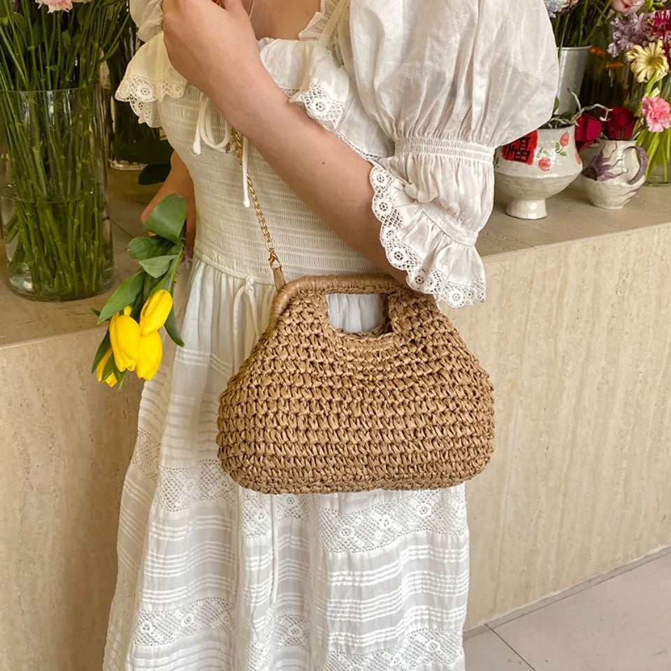 Person holding a woven handbag with flowers, wearing a white dress, in a home setting.