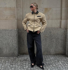 Person wearing a beige jacket with black accents against a stone wall.