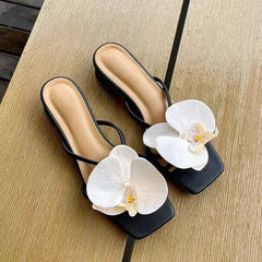 Black high-heeled sandals with white orchids on a wooden surface