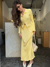 Woman in a yellow outfit holding a white handbag in an indoor setting.