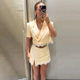Woman wearing a pale yellow lace-trimmed blazer and mini skirt set