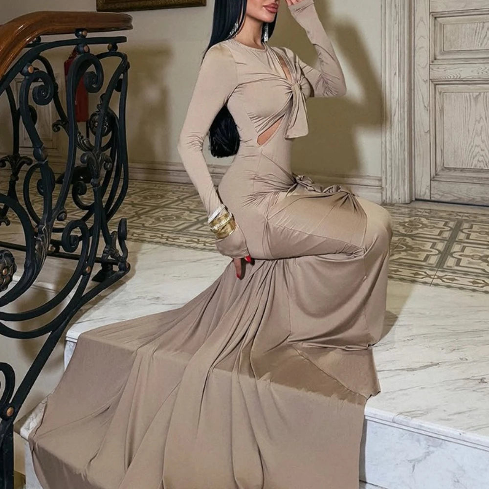 Woman in a beige evening gown sitting on a staircase in an elegant interior setting.