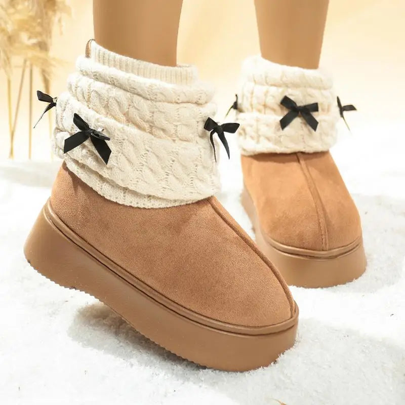 Tan snow boots with white fuzzy trim and black bows on a snowy background