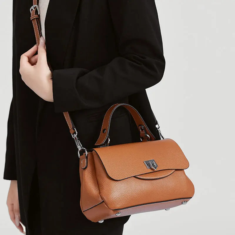 Brown leather handbag held by a person wearing a black coat on a light gray background