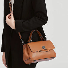 Brown leather handbag held by a person wearing a black coat on a light gray background