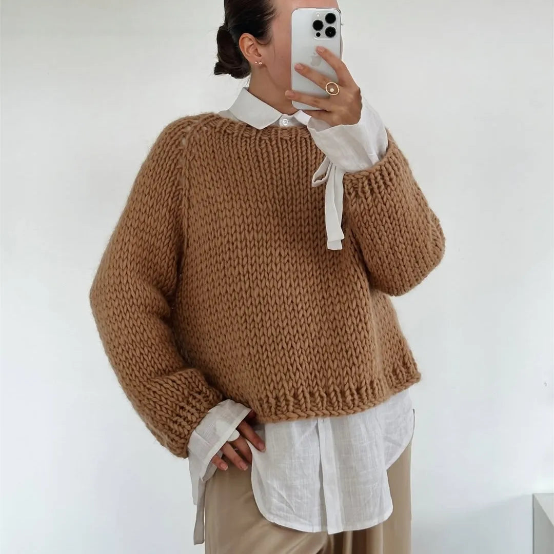 Person wearing a brown knitted sweater over a white shirt with a plain background