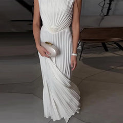 Woman in a white pleated dress holding a clutch in an indoor setting